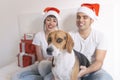 young couple sitting on bed with christmas santa hats having fun with their dog. Presents on bed. Home, indoors. Xmas concept Royalty Free Stock Photo