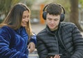 Young couple sitting on the bench in a square with mobile phone and headphones Royalty Free Stock Photo