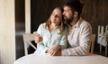 Young couple sitting at cafe table near window, bearded man hugging woman wife in restaurant, date and romance Royalty Free Stock Photo