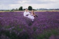 Young couple are sitting on chairs at table and relaxing in lavender field. woman in purple dress and flower`s wreath with man