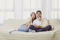 A young couple sitting on the couch watching an interesting TV . Royalty Free Stock Photo