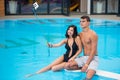 Young couple sitting on the edge of the swimming pool and taking selfie photo on the phone with selfie stick Royalty Free Stock Photo
