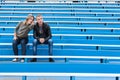 Young couple sitting on empty stadium sector on competition. Woman pointing and explaining the man with arms