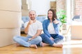 Young couple sitting on the floor arround cardboard boxes moving to a new house doing happy thumbs up gesture with hand Royalty Free Stock Photo