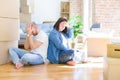 Young couple sitting on the floor arround cardboard boxes moving to a new house suffering from headache desperate and stressed Royalty Free Stock Photo