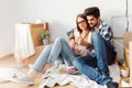 Young couple sitting on the floor of empty apartment looking at smart phone. Move in to new home. Royalty Free Stock Photo