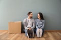 Young couple sitting on floor near box indoors. Moving into new house Royalty Free Stock Photo