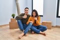 Young couple sitting on the floor at new home doing happy thumbs up gesture with hand Royalty Free Stock Photo