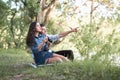 Young couple sitting on the grass in the forest, taking photos and looking on sunset, summer nature, bright sunlight, shadows and Royalty Free Stock Photo
