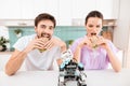 A young couple is sitting in the kitchen. They eat sandwiches. A small rhino-rhino is sitting next to it.