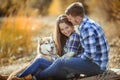 A young couple is sitting by the lake at sunset with a Husky breed dog. Royalty Free Stock Photo