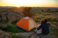 Young Couple Sitting near Tent and Watching Beautirul Sunset in the Mountains. Adventure and Family Travel.