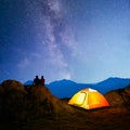 Young Couple Sitting on the Rock near Illuminated Tent and Watching the Bright Milky Way Above the Beautiful Mountains Royalty Free Stock Photo