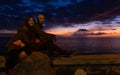 Young couple sitting on rock posing at beautiful sunset by the sea Royalty Free Stock Photo