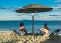 Young couple sitting on a sand and looking to a sea under umbrella. Summer relax on beach. Royalty Free Stock Photo