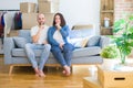 Young couple sitting on the sofa arround cardboard boxes moving to a new house asking to be quiet with finger on lips