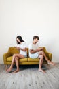 Young couple sitting on sofa back to back using mobile phones Royalty Free Stock Photo