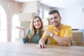 Young couple sitting on the table movinto to new home with carboard boxes behind them amazed and smiling to the camera while Royalty Free Stock Photo
