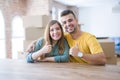 Young couple sitting on the table movinto to new home with carboard boxes behind them doing happy thumbs up gesture with hand Royalty Free Stock Photo