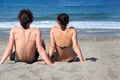 Young couple sitting together on a sand by sea and looking to a horizon. Royalty Free Stock Photo