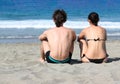 Young couple sitting together on a sand by sea and looking to a horizon. Royalty Free Stock Photo