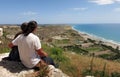 A young couple sitting on top of a cliff looking at the Mediterranean sea