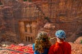 Young couple sitting at a viewpoint on Al Khazneh tomb also called Treasury at Petra, Jordan