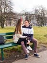 Young couple sitting on a wooden bench. Beautiful sunny day. Young happy people relaxing outdoor in the park. They are looking at Royalty Free Stock Photo