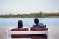 A young couple is sitting on a wooden bench with pillows on the sandy river bank and enjoying the scenery. A married man and woman Royalty Free Stock Photo