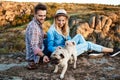 Young couple smiling, sitting on rock in canyon, stroking pug dog. Royalty Free Stock Photo