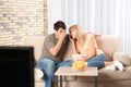 Young couple with snacks watching TV on sofa