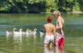 A young couple stand knee deep in river as geese float by