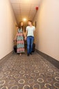Young couple standing at hotel corridor upon arrival, looking for room, holding suitcases.
