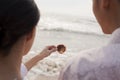 Young couple standing and looking at seashell on the beach, over the shoulder view Royalty Free Stock Photo