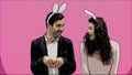 Young couple standing standing on pink background. During this time, they are dressed in rabble ears. Looking at each