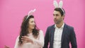 Young couple standing standing on pink background. During this time, they are dressed in rabble ears. Looking at each