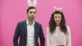 Young couple standing standing on pink background. During this time, they are dressed in rabble ears. Looking at each