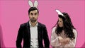 Young couple standing standing on pink background. During this time, they are dressed in rabble ears. Looking at each