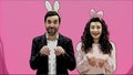 Young couple standing standing on pink background. During this time, they are dressed in rabble ears. Looking at each