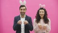 Young couple standing standing on pink background. During this time, they are dressed in rabble ears. Looking gently at