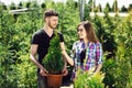 Young couple standing together, holding a pot with a small fir tree and looking at a plant in the garden center Royalty Free Stock Photo