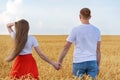 Young couple standing in wheat field and holding hands. Back wiev Royalty Free Stock Photo