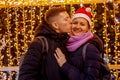 Young Couple Stands Embracing Against The Shining Festive Garlands.