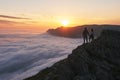 Young couple stands in the mountains above the clouds and looks at beautiful sunset view Royalty Free Stock Photo