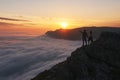 Young couple stands in the mountains above the clouds and looks at beautiful sunset view Royalty Free Stock Photo