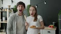 Young couple stared at the camera, standing in surprise in the kitchen at home