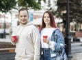 A young couple of students in love - a beautiful girl and a nice guy on the street with cups of coffee in the summer. Royalty Free Stock Photo