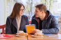 Young couple of students study in outdoor cafe, drink coffee tea, eat croissants, background is spring city street Royalty Free Stock Photo