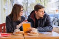 Young couple of students study in outdoor cafe, drink coffee tea, eat croissants, background is spring city street Royalty Free Stock Photo