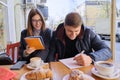 Young couple of students study in outdoor cafe, drink coffee tea, eat croissants, background is spring city street Royalty Free Stock Photo